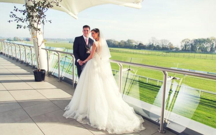 Newlywed couple standing on a balcony at Bath Racecourse.