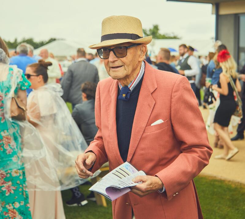 A dapper older gentleman holding a horse race card at Bath Racecourse