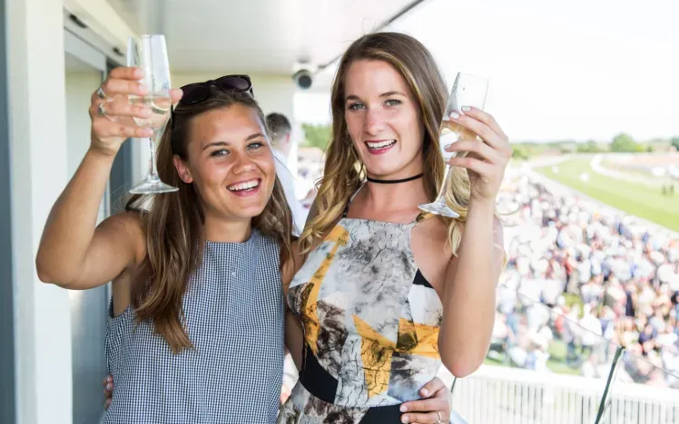 Two race guests at Bath hold up glasses of champagne