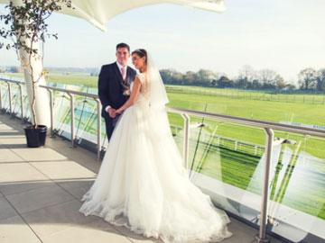 Newlywed couple standing on a balcony at Bath Racecourse.