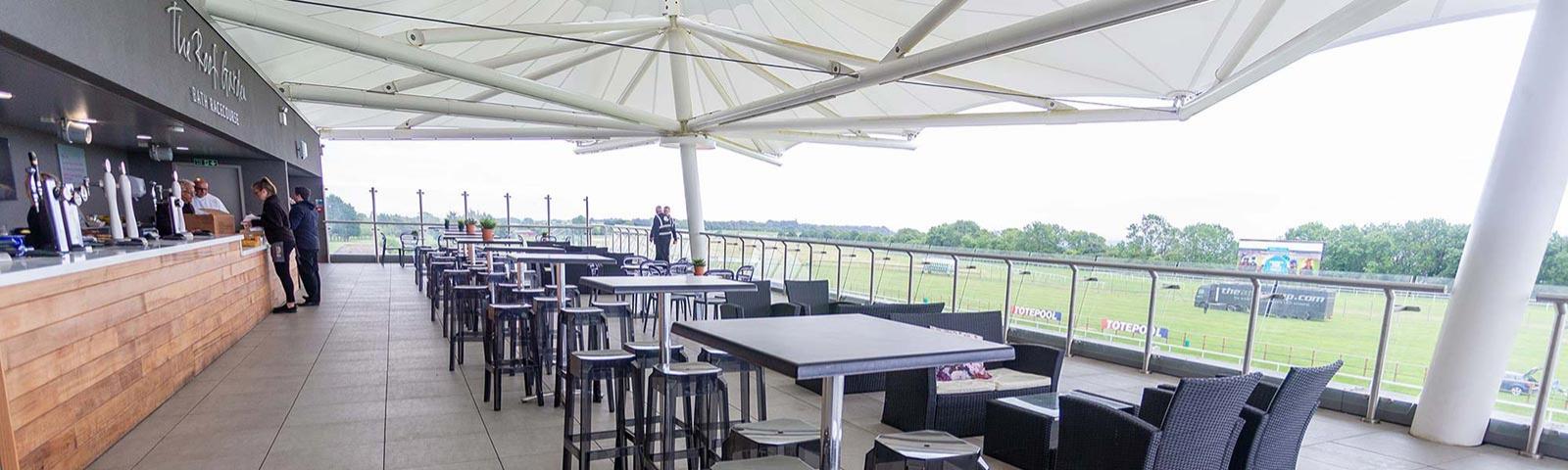 View of the Roof Garden bar at Bath Racecourse, with rows of tables set up alongside the bar.