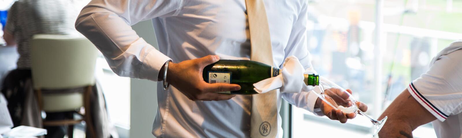A member of waiting staff at Bath Racecourse pouring a glass of bubbly