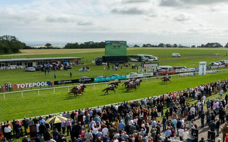 Jockeys racing past the crowds at Bath Racecourse.