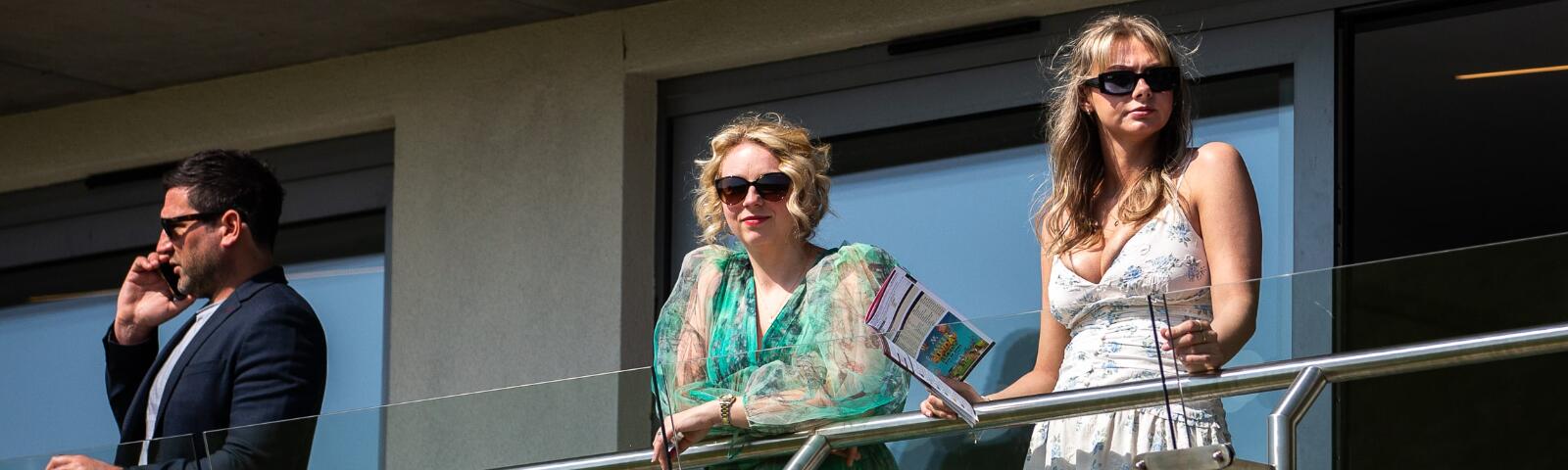 Two hospitality guests holding a horse race card on the balcony at Bath Races