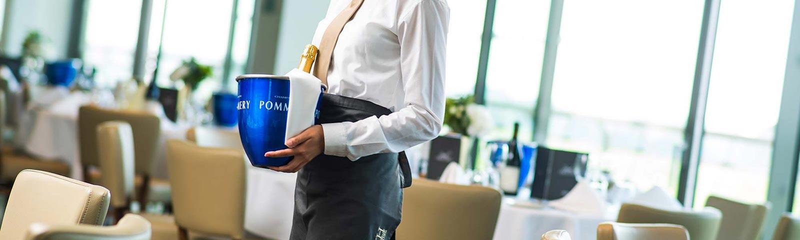 Waitress carrying a bucket with a bottle of champagne inside.