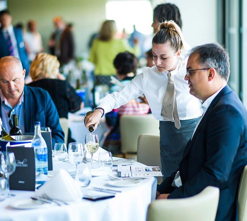 Waitress pouring champagne for a guest sitting at a table.