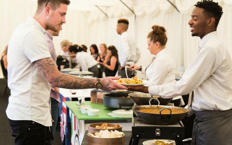 Waiter passing a plate full of food to a racegoer.