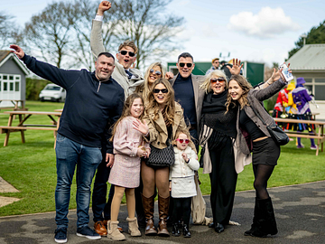 Family smiling with their arms in the air at the front of Bath Racecourse 